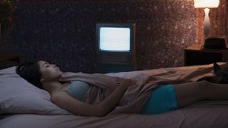 woman sleeping in bed with TV and bedside lamp on