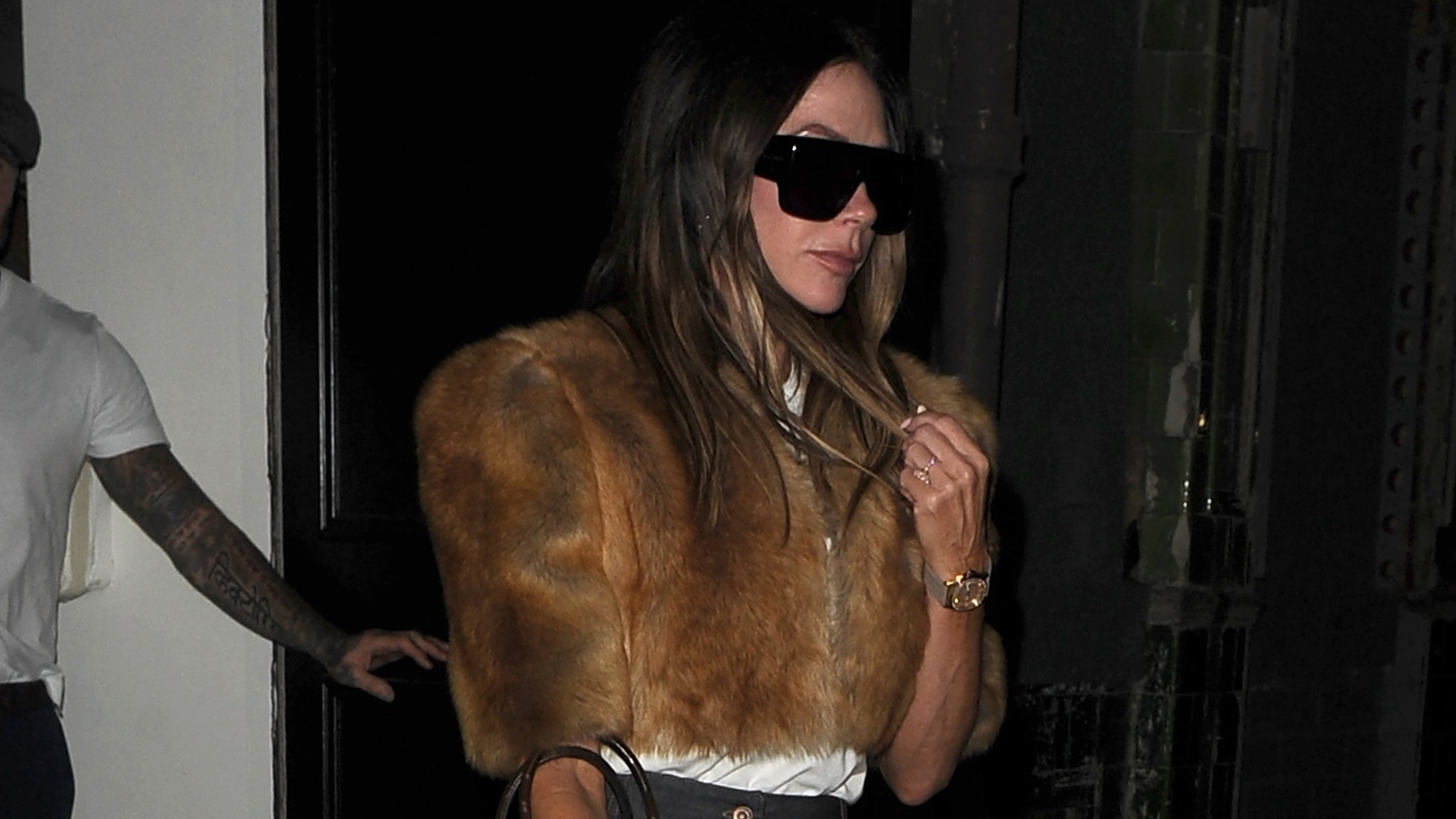 Victoria Beckham wears oversize sunglasses and a cropped fur jacket.