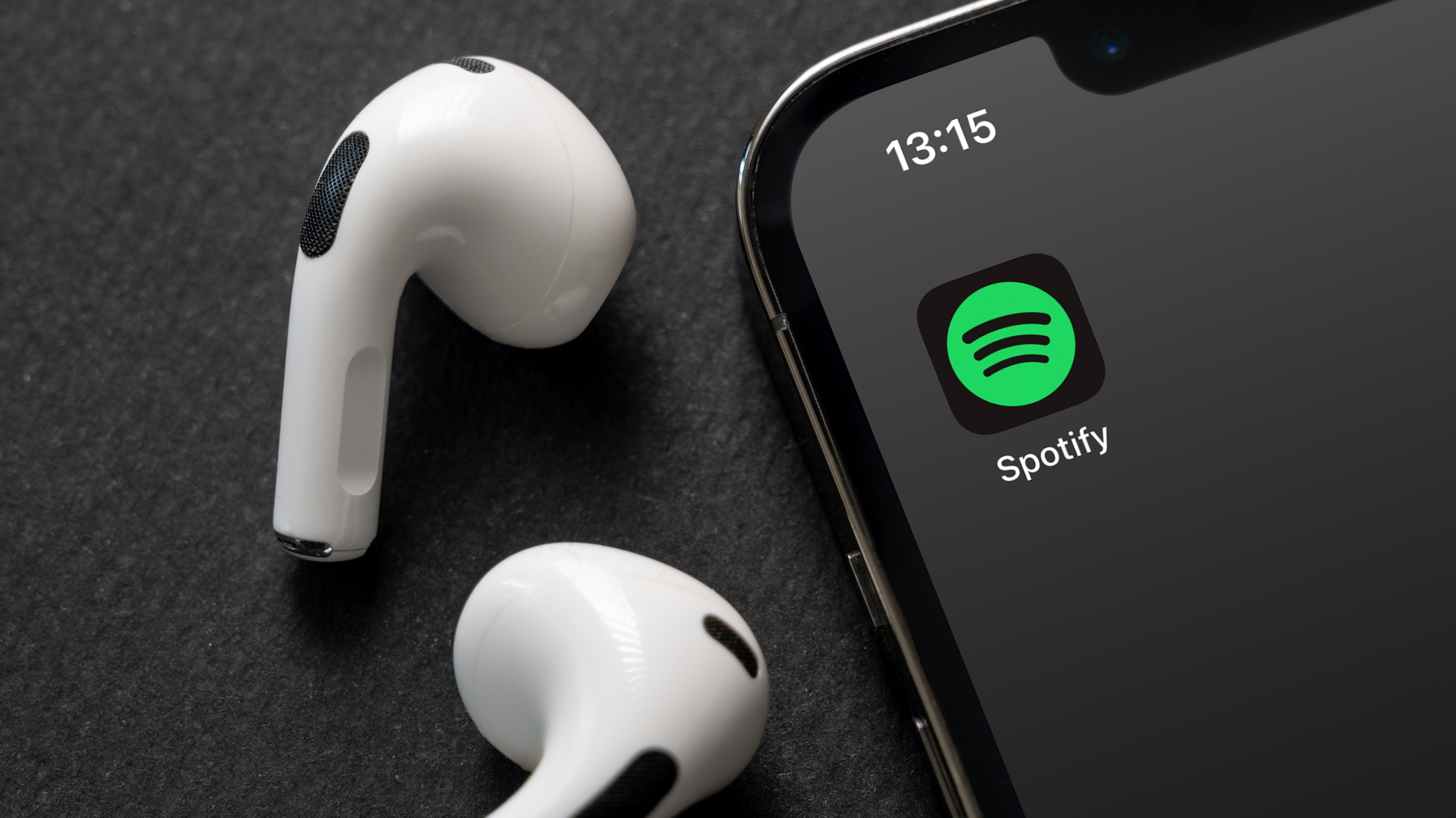 iPhone smartphone screen showing Spotify Music App logo next to two AirPods 
