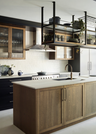 Wooden kitchen island with a sink built into the centre. Behind are wooden, glass fronted cabinets and black built in cabinets.