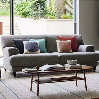 bright living room with grey sofa with an assortment of cushions in front of floor to ceiling glass windows