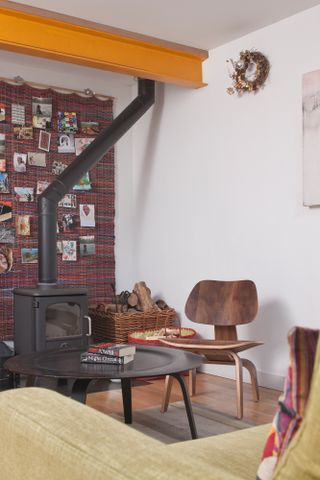 Stove in a living room with yellow metal ceiling beam, wooden chair and black coffee table