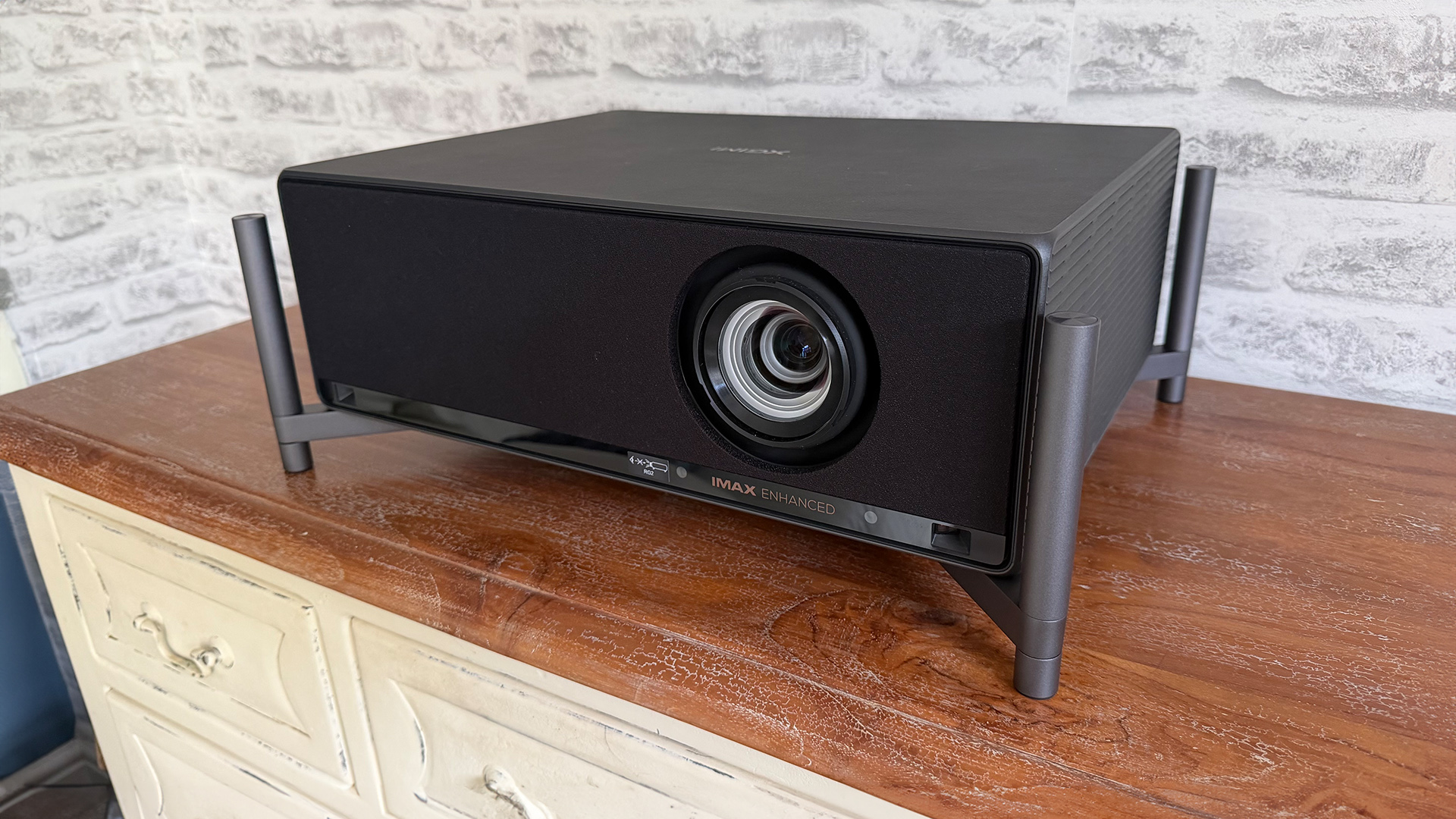 Xgimi Titan home cinema projector on wooden sideboard in front of white brick wall