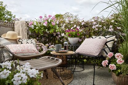A balcony with outdoor garden furniture and decorated with different colored geraniums in pots
