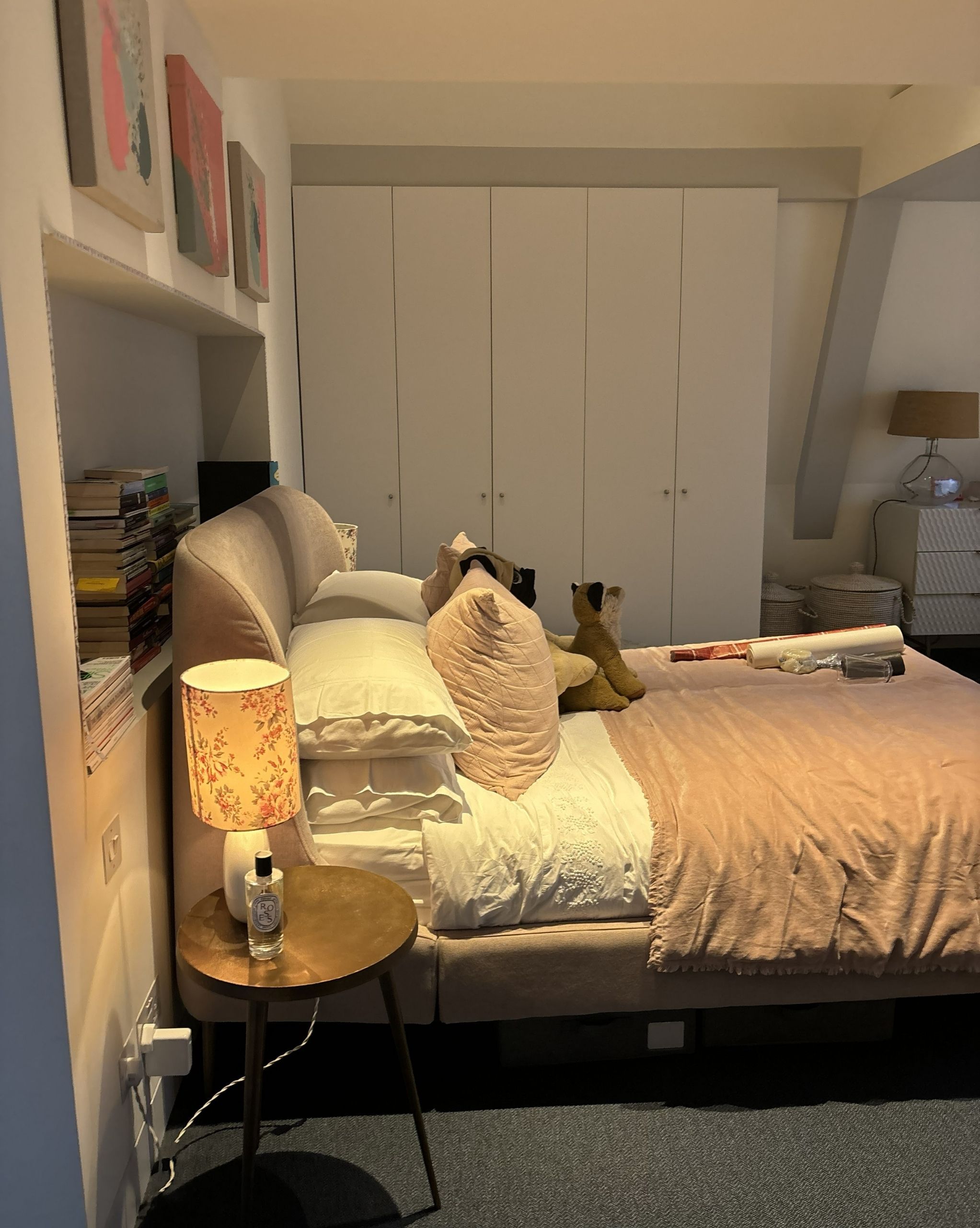 Image of a bedroom with navy carpets, white walls, and a light pink bed with white and light pink bedding. 