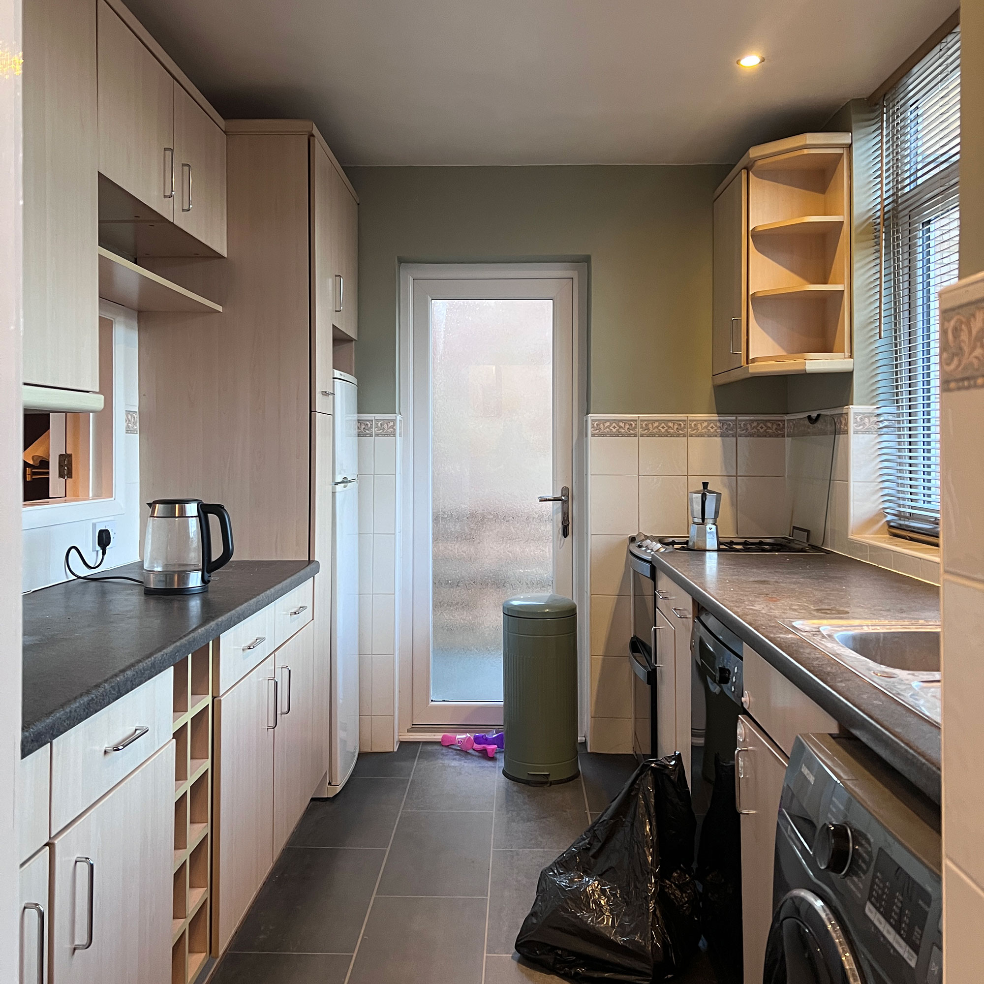 Kitchen pre-renovation with half-tiled walls, spotlights and wooden cabinetry