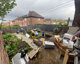 a messy backyard before a makeover, with plants, tools and mud scattered around