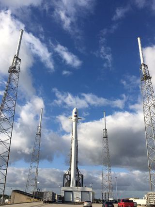 A long, slim rocket points toward the sky between four tall metal framework towers.