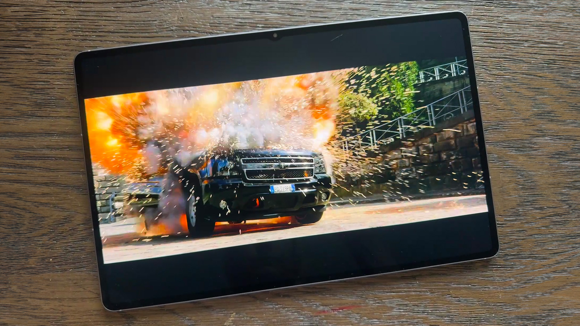 Samsung Galaxy Tab S11 Ultra tablet on wooden table, on screen is car exploding