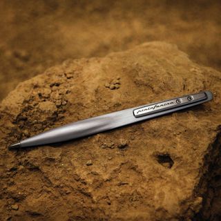 A metallic pen with a futuristic finish stands against a rocky, brown surface.