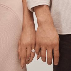 A close up of two people touching hands side by side, with one of the people wearing a diamond engagement ring from Peoples.