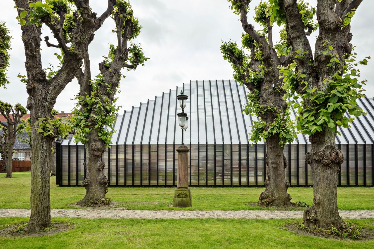 Daytime, outside image of Fritz Hansen pavilion, green lawn, stone cobble pathway, trees, stone based lighting, cloudy sky