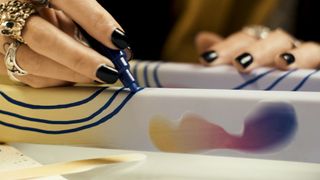 An artist is shown close up drawing on the forks of a bike