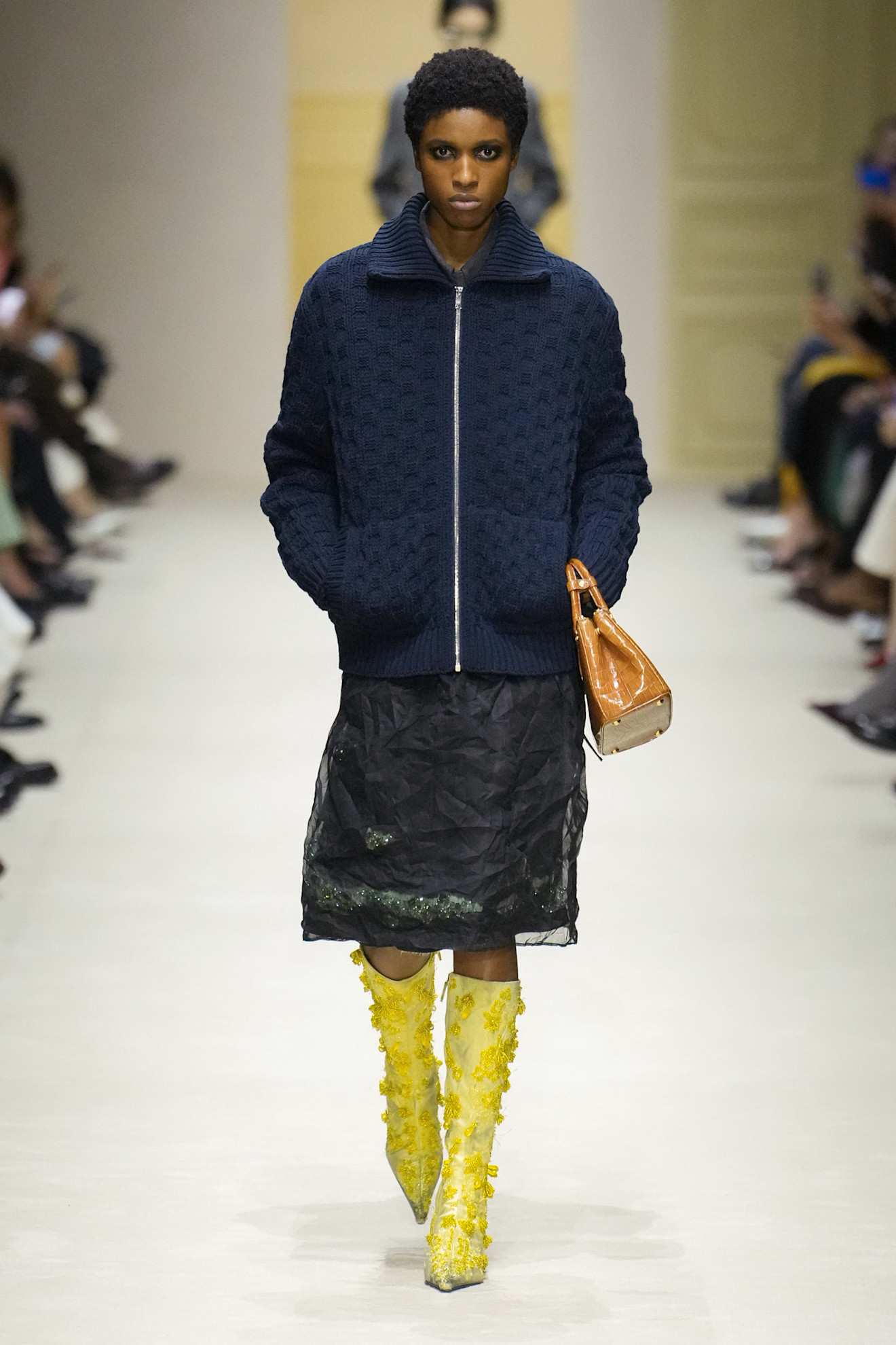 A model at the F/W 26 Prada show wearing a chunky knit sweater with a sheer pencil skirt.