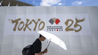 A man shields himself from the hot sun with an umbrella as he walks past an advertisement of the 2025 World Athletics Championships, which will take place from September 13-21, outside the National Stadium in Tokyo on September 6, 2025.