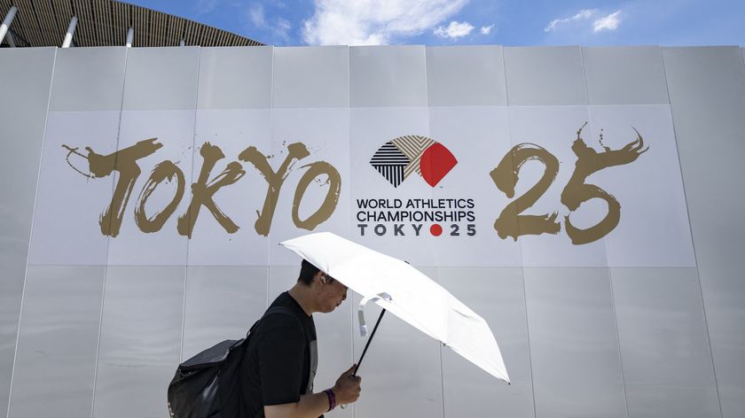 A man shields himself from the hot sun with an umbrella as he walks past an advertisement of the 2025 World Athletics Championships, which will take place from September 13-21, outside the National Stadium in Tokyo on September 6, 2025. 