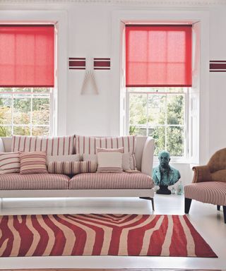 White living room, beige sofa striped cushions and bolsters, sash windows, red blinds, rug