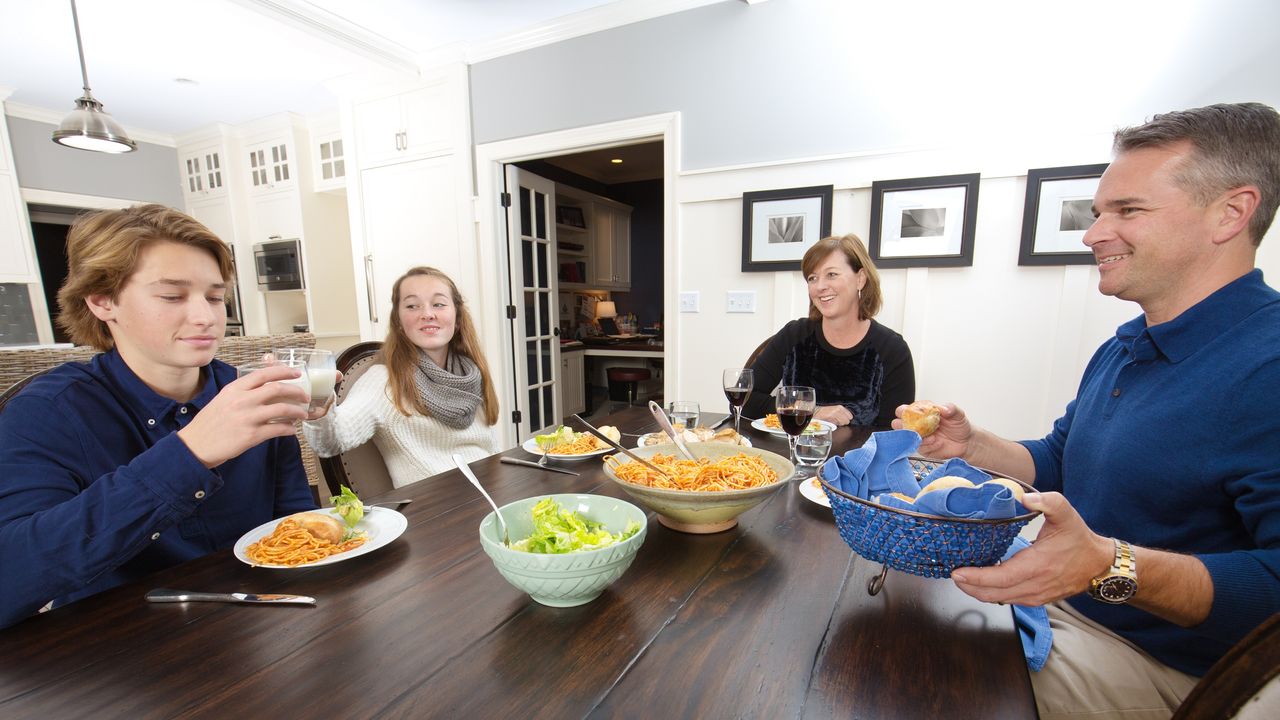 Parents and two teenagers talk while having dinner.