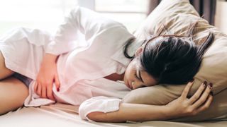 woman lying on her bed with stomach pain