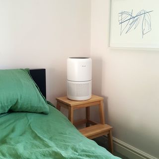 The Levoit Core 300S air purifier on a bedside table in a pale pink bedroom with green bedding