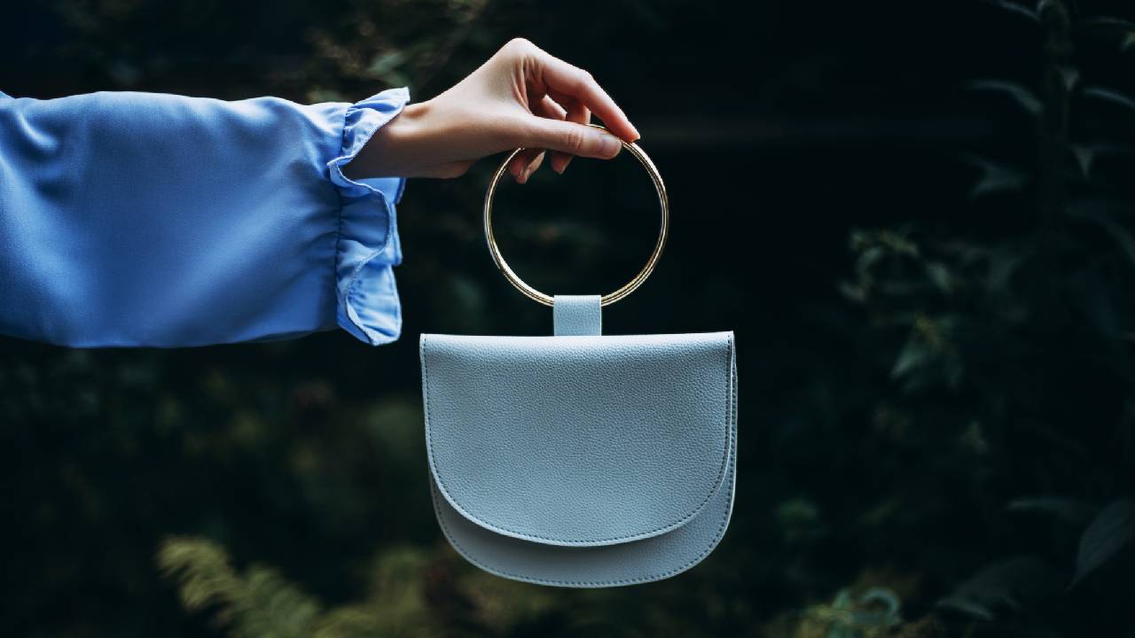 A woman wearing a blue, satin, long-sleeve top, holding a light blue bag. 