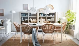 White, modern dining space with rattan contrast chairs, jute rug, and white lighting, with glass-fronted dressers in background.