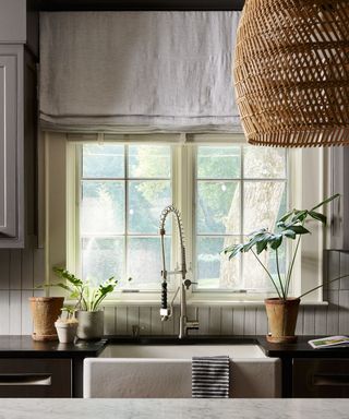 A kitchen with gray drapes, a rattan light fixture, and a light green window