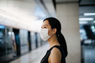 Vaccine misinformation: Asian woman with protective face mask waiting for subway MTR train in platform