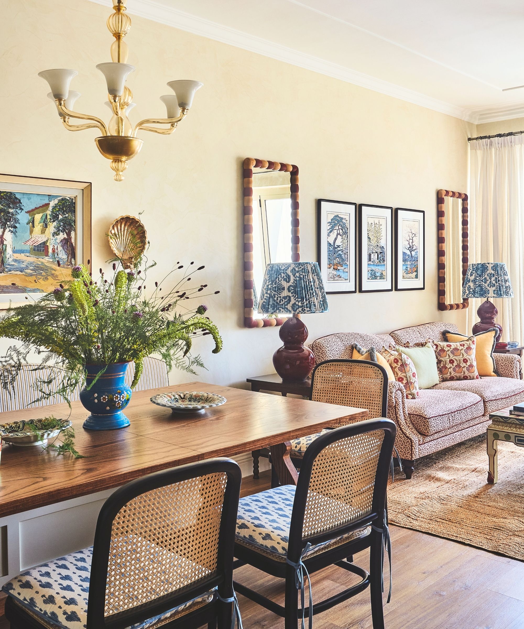 living room with patterned sofa and armchair and textured seagrass rug and colourgul painted wooden coffe table and art on walls behind with symmetrical mirrors