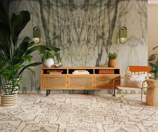 large grey and white marble bookmatched wall panels in living room with cream and black patterned rug, plants, orange chair and wood and wicker low sideboard