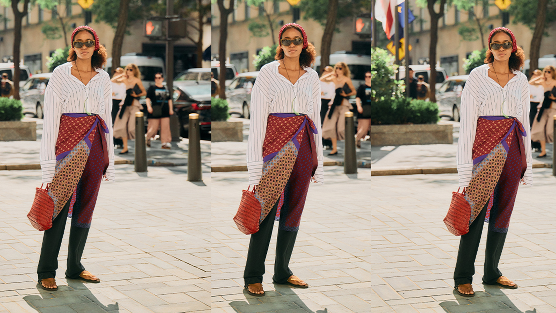 Naomi wears white button down, black trousers, red bandana, red braided handbag, flat sandals, and a scarf around her waist. 
