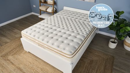 The Saatva Classic luxury innerspring hybrid mattress, on sale this Presidents' Day, is shown here on a white wooden bed frame in our blue Tom's Guide Sleep Product Testing Lab, with a blue Presidents' Day deals badge overlaid in the top right hand corner