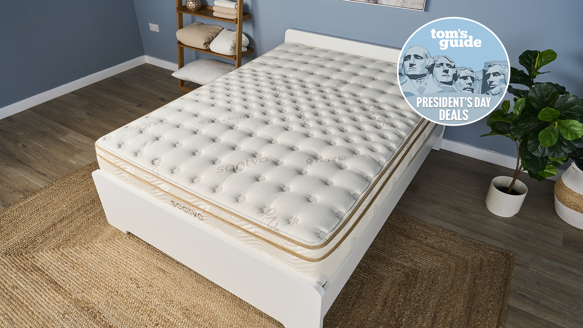 The Saatva Classic luxury innerspring hybrid mattress, on sale this Presidents' Day, is shown here on a white wooden bed frame in our blue Tom's Guide Sleep Product Testing Lab, with a blue Presidents' Day deals badge overlaid in the top right hand corner