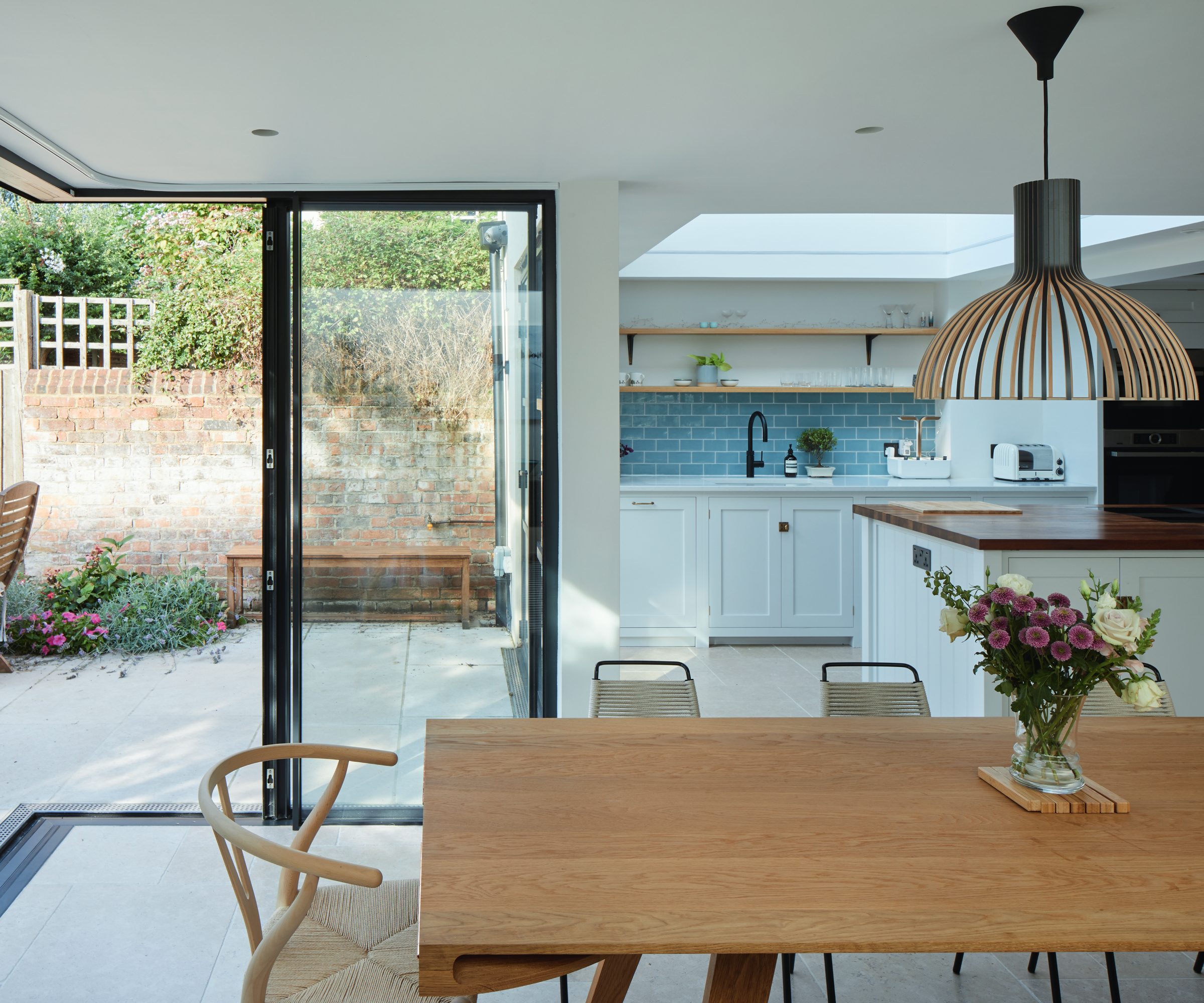 kitchen with corner opening glazed doors, wooden table and chairs, large rooflight above kitchen island