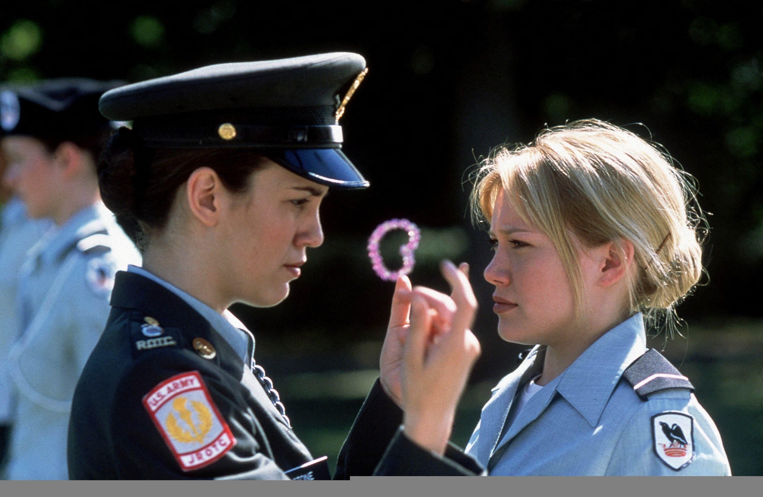 christy carlson romano wears a cadet uniform and holds a pink hair tie in front of hilary duff's face in a still from the disney channel original movie cadet kelly