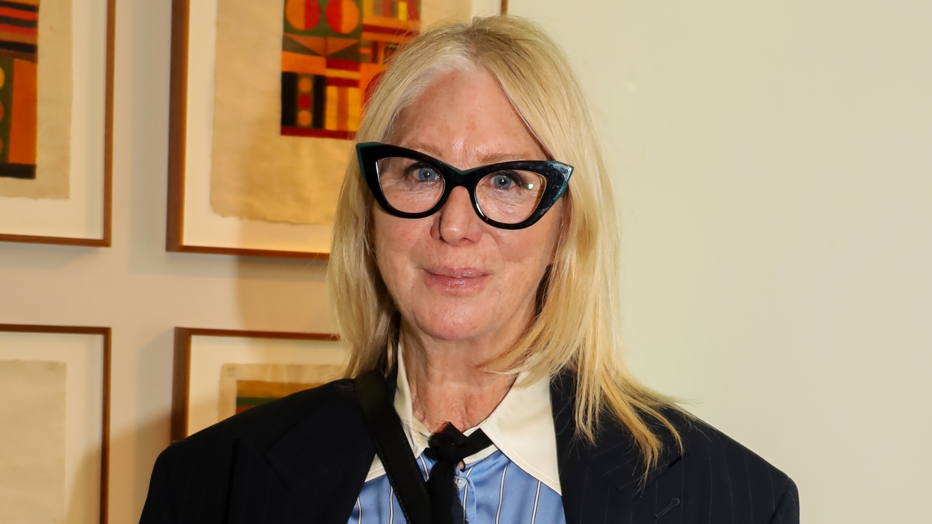 Image of Val Garland smiling with straight, side part blonde shoulder-length hair and wearing black cat-eye frame glasses