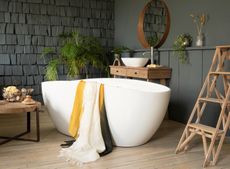 Luxury bathroom ideas White freestanding bathtub on light wooden floor with dark grey textured walls, wooden ladder and side table