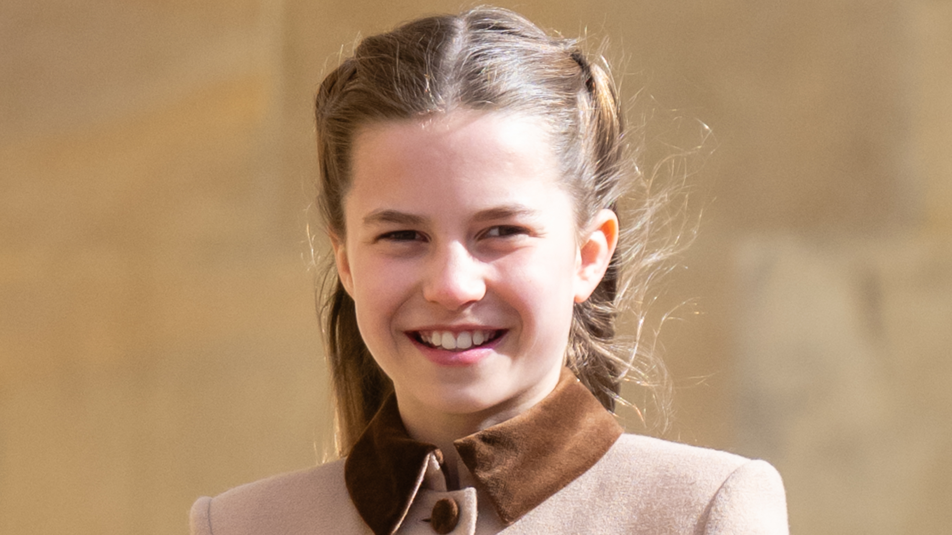 Princess Charlotte wears a light brown coat with a dark collar and smiles