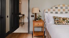 a pale light blue bedroom with dark navy painted trim and doors with a patchwork yellow headboard, wooden nightstand, and a marble print pillow