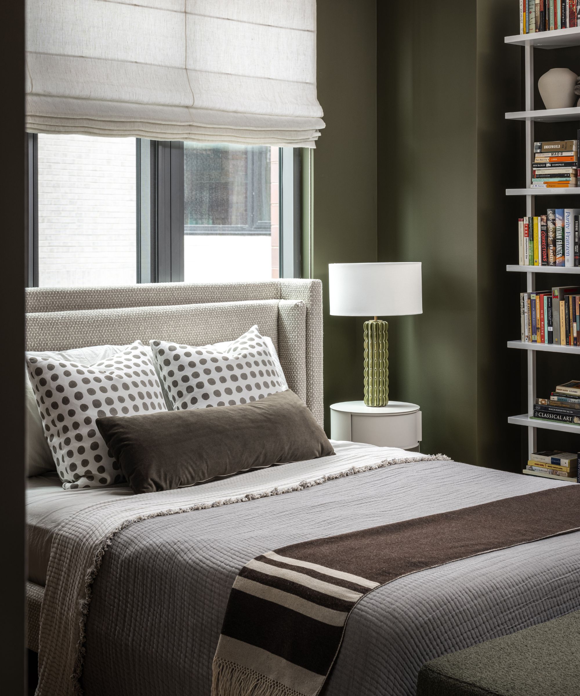bedroom with dark green walls, a bed in front of the window with gray bedding and patterned cushions