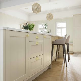 kitchen with pendant lights, cashmere cabinets with gold handles, grey stools and wooden flooring