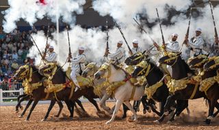 A line of horsemen performs T&#039;bourida (Fantasia) during the Horse Show of El Jadida, while firing muskets, creating rising smoke in the air 