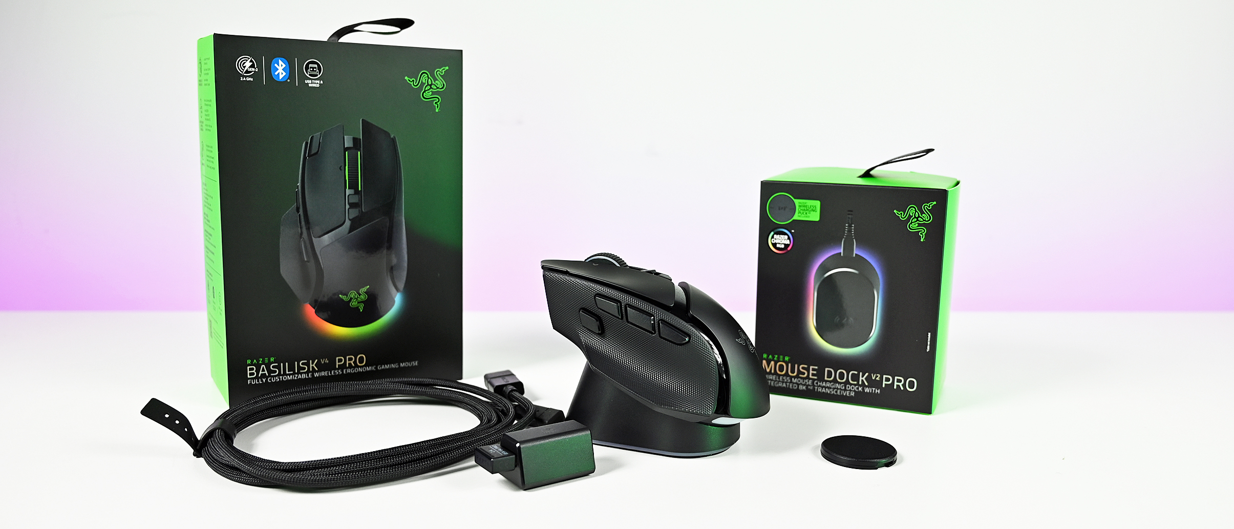 Wide studio shot of the Razer Basilisk V4 Pro mouse on its charging dock, flanked by retail packaging, USB cable, and wireless dongle.
