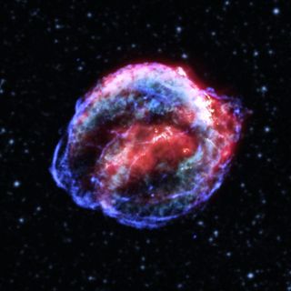 The full view of Kepler's supernova remnant with all filters included. There are brilliant shades of pink, blue and various other colors. The remnant is seen in the center of the image with a background of space speckled by stars and galaxies, shown as bright dots.