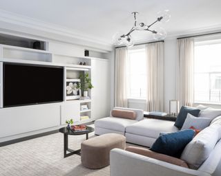 A family room with a full wall of open and closed cabinetry and large low corner sofa in pale grey
