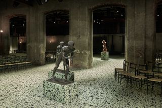 Image of Bottega Veneta show space featuring bronze scuptures of runners in the foreground and a futurist sculpture in the background