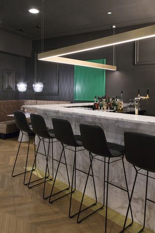The Fritz cocktail bar with white marble bar and black stools, wooden flooring and grey wall panelling