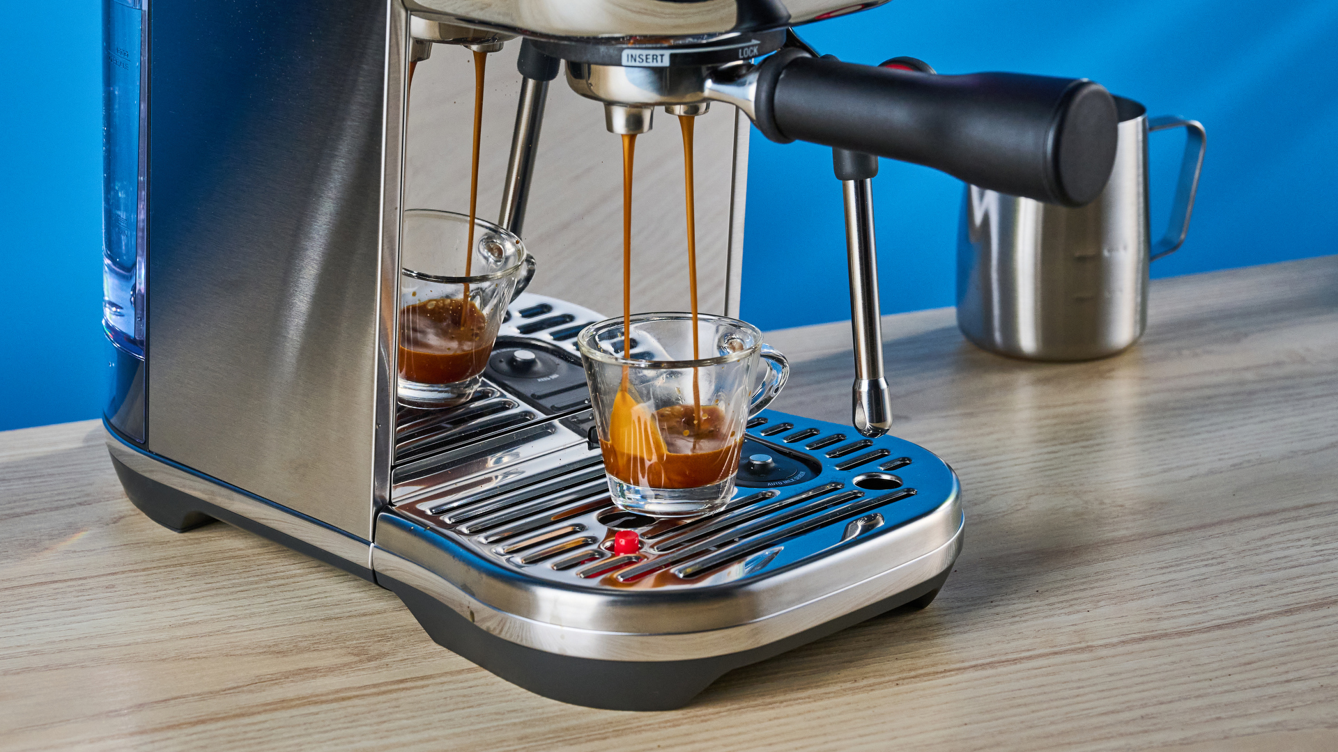the breville bambino plus / sage bambino plus in stainless steel silver photographed against a blue background shown with its accessories including milk jug, tamper, portafilter, and shown in use extracting espresso
