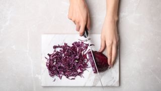 A knife cutting a red cabbage on a marble cutting board
