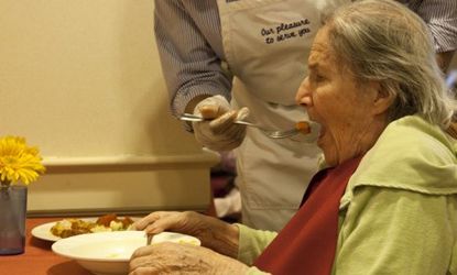 A woman at an Alzheimer's residence gets help with dinner
